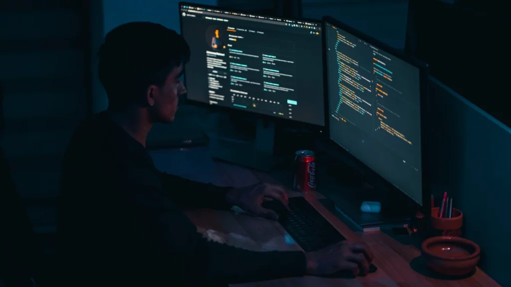 Software developer coding in a dark room on two monitors
